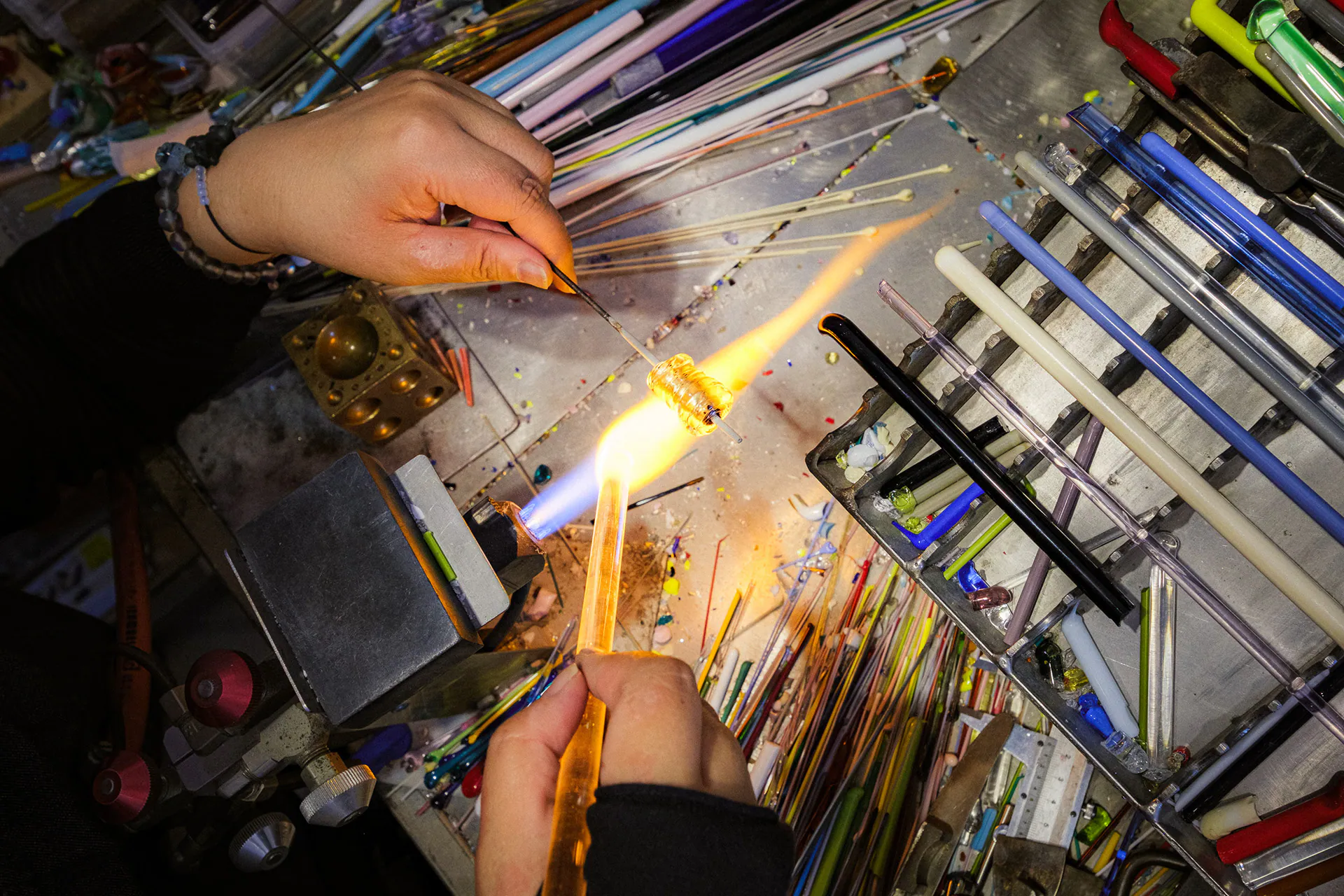 Le mani di un’artigiana lavorano il vetro alla fiamma, fotografate con un grandangolo a Murano