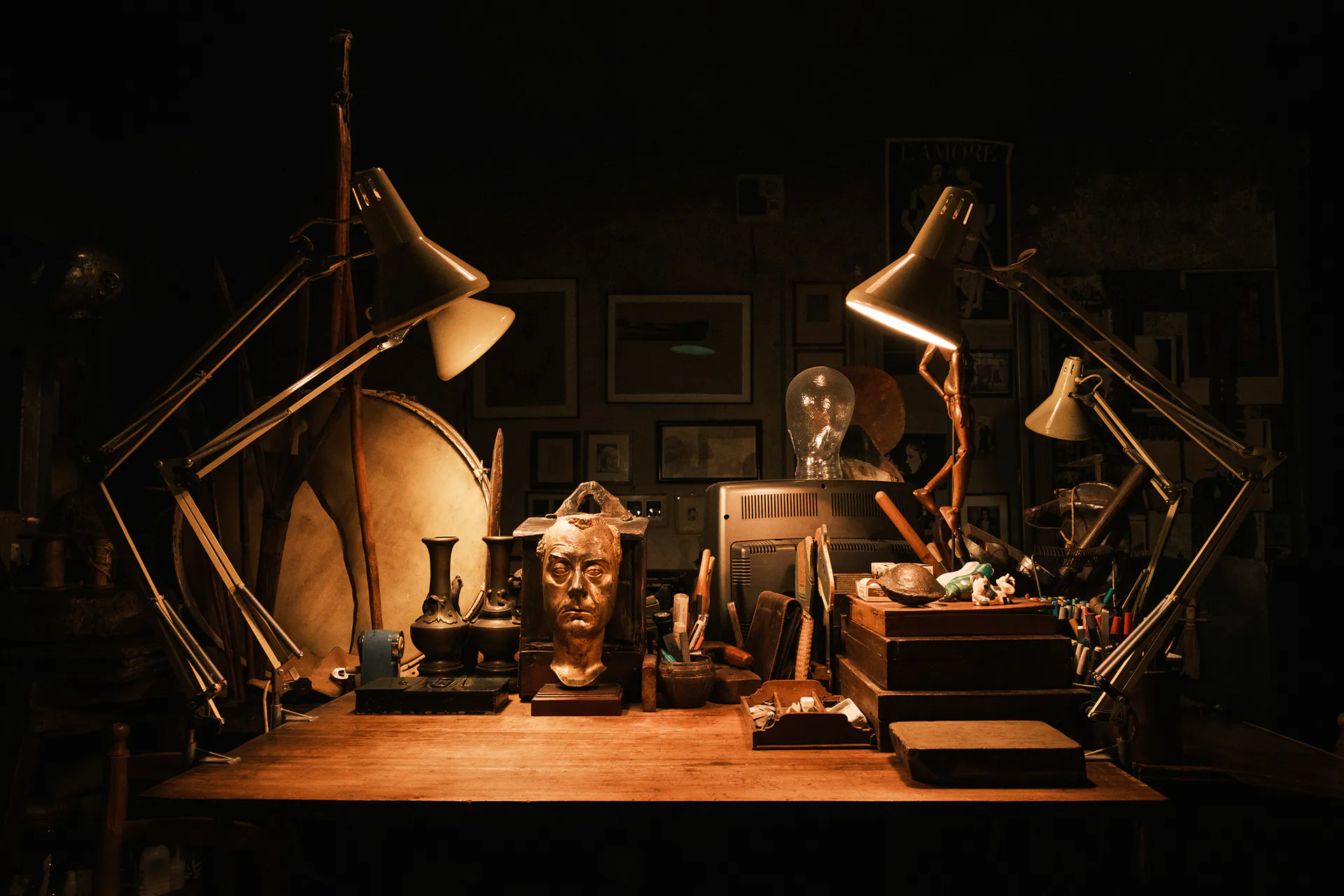 Tavolo di lavoro con lampade, oggetti e sculture nella penombra della casa di Carol Rama.