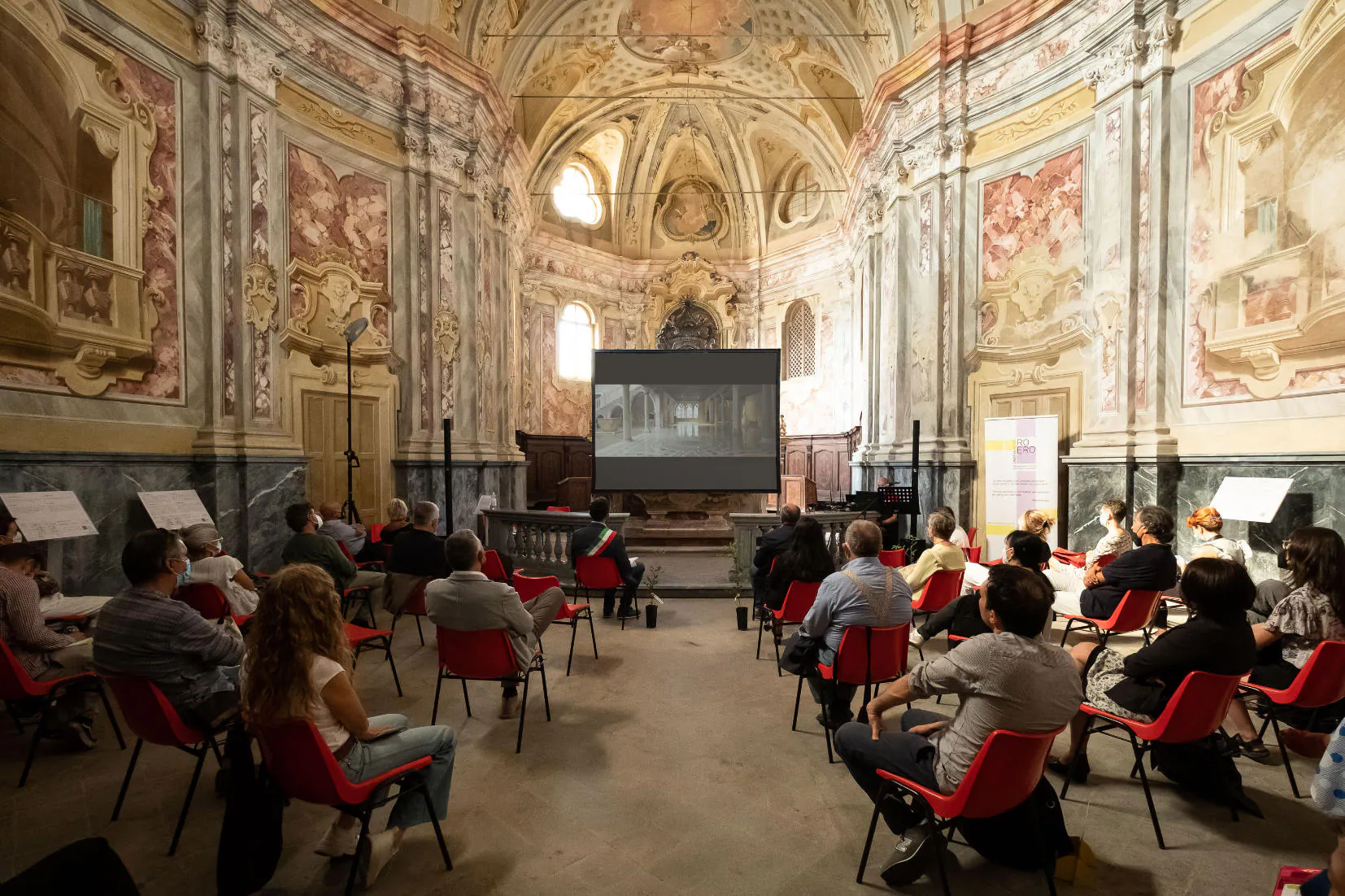 Il pubblico in una chiesa affrescata durante la proiezione del docufilm