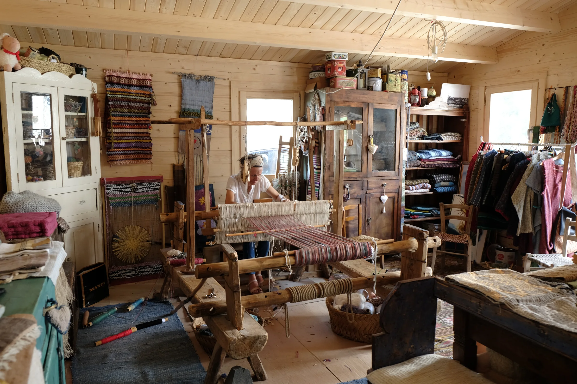 Assunta seated at the wooden loom, surrounded by fabrics and tools in her workshop