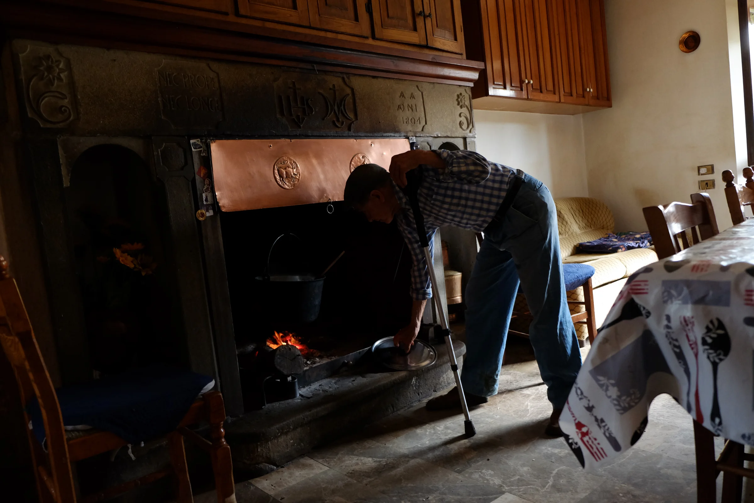 A man bending over the lit kitchen fireplace