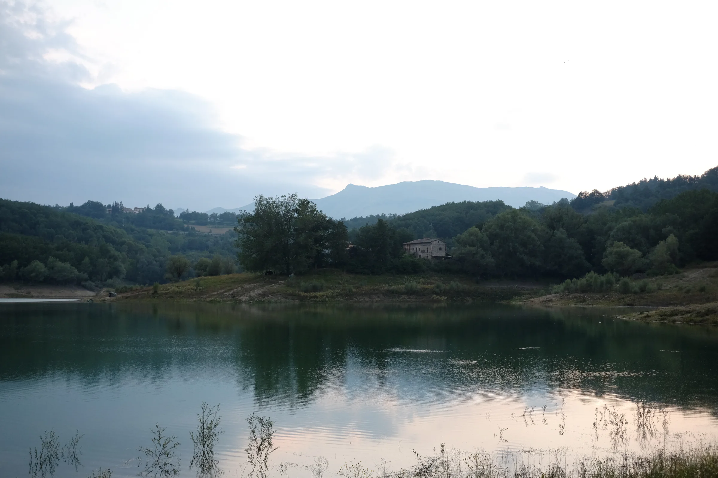 Lake Scandarello at dusk, with a house among the trees and mountains behind
