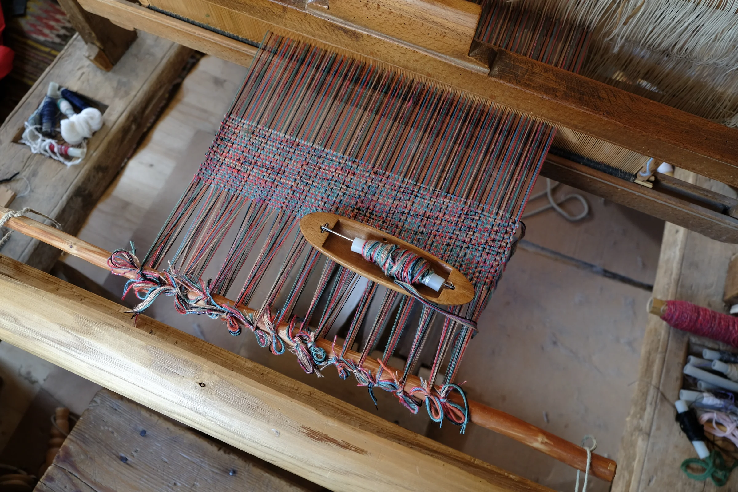 A wooden shuttle resting among the threads of a red, blue and green fabric