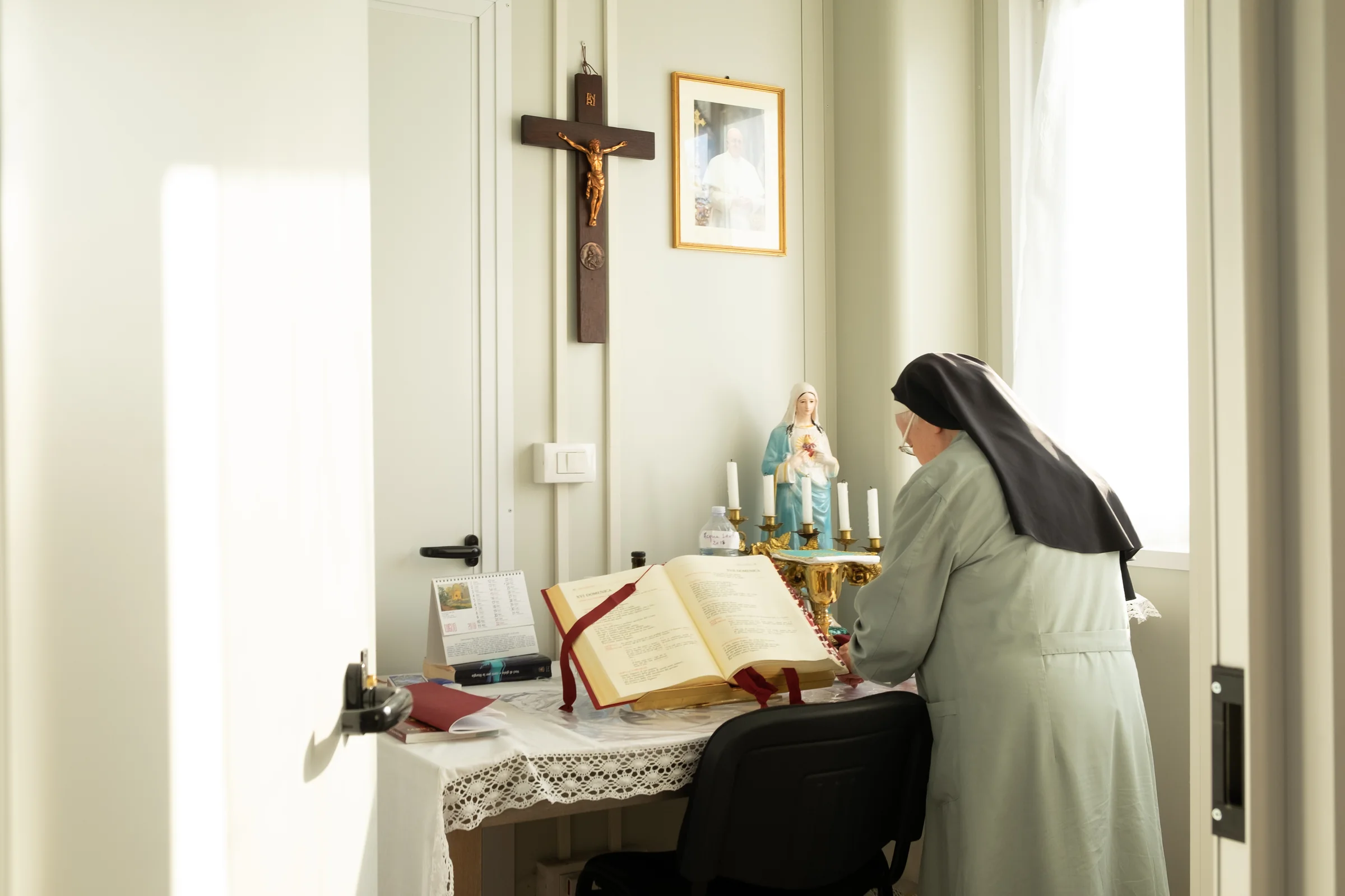 A nun preparing the missal on a simple altar, in a bright room