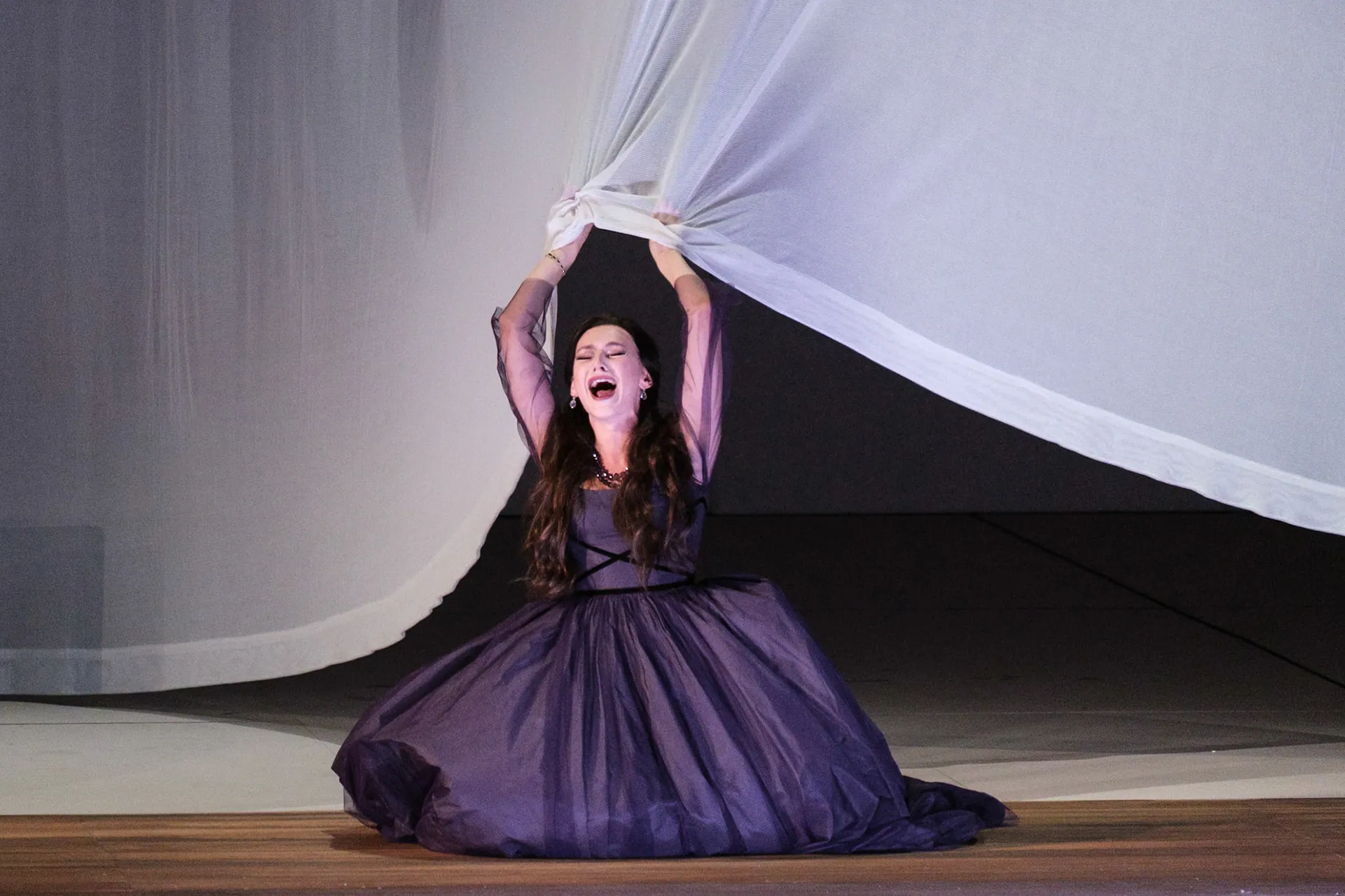 Francesca, in abito viola, solleva una grande tenda bianca al centro della scena.