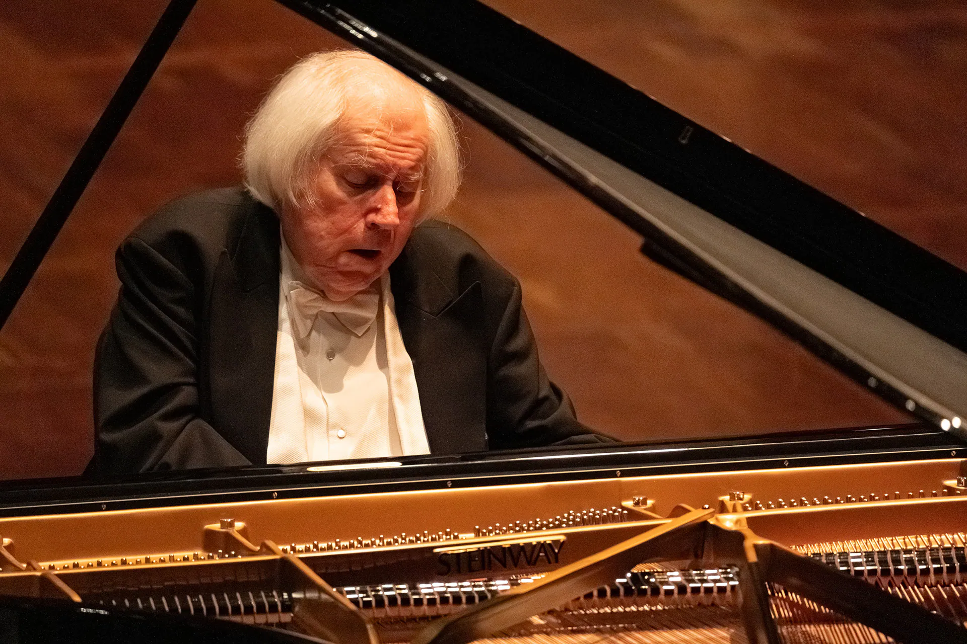 Grigory Sokolov al pianoforte, in primo piano, illuminato nella sala buia.