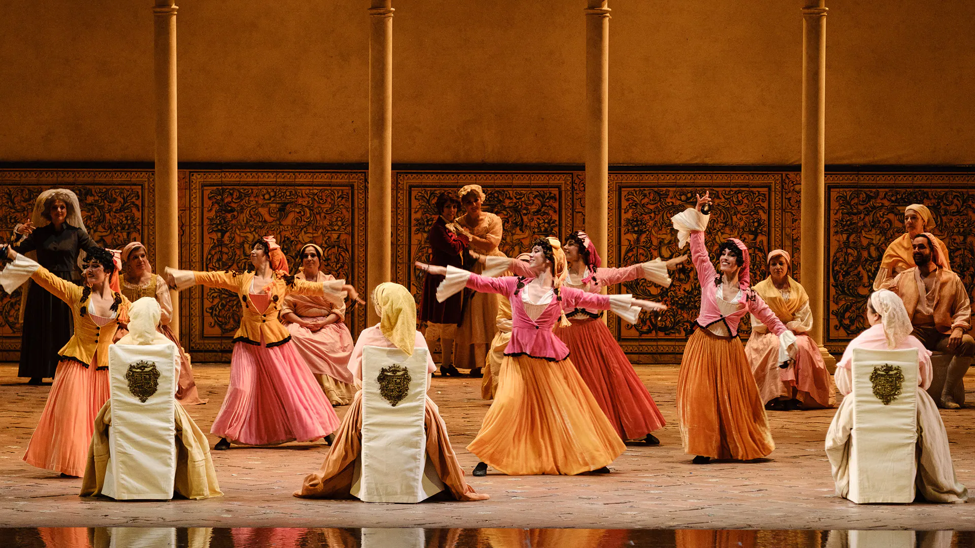 Scena d’insieme de Le nozze di Figaro: il coro in costumi settecenteschi danza su un palco dai toni caldi.