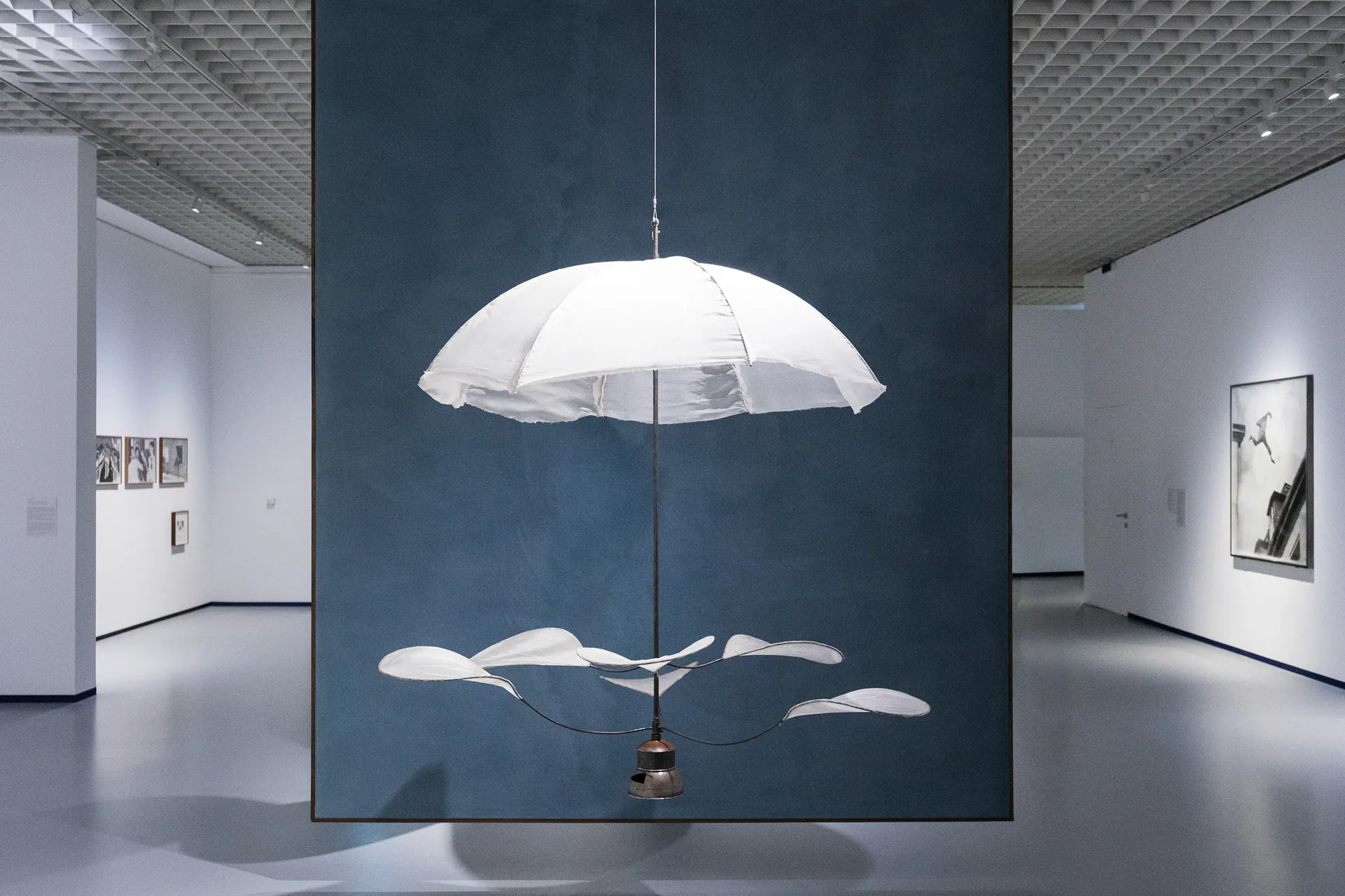 Installation with a white umbrella suspended in front of a blue wall, in Linda Fregni Nagler’s exhibition at GAM Torino.