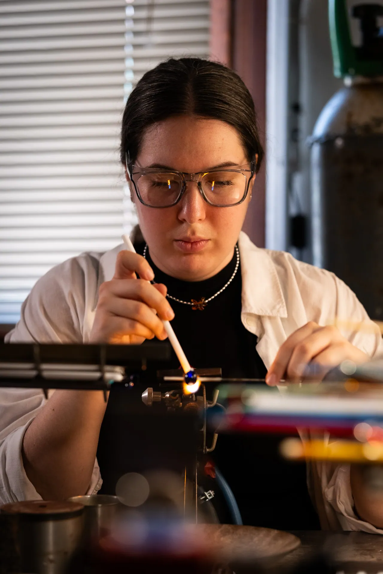 Portrait of a young artisan in a white coat working a blue bead