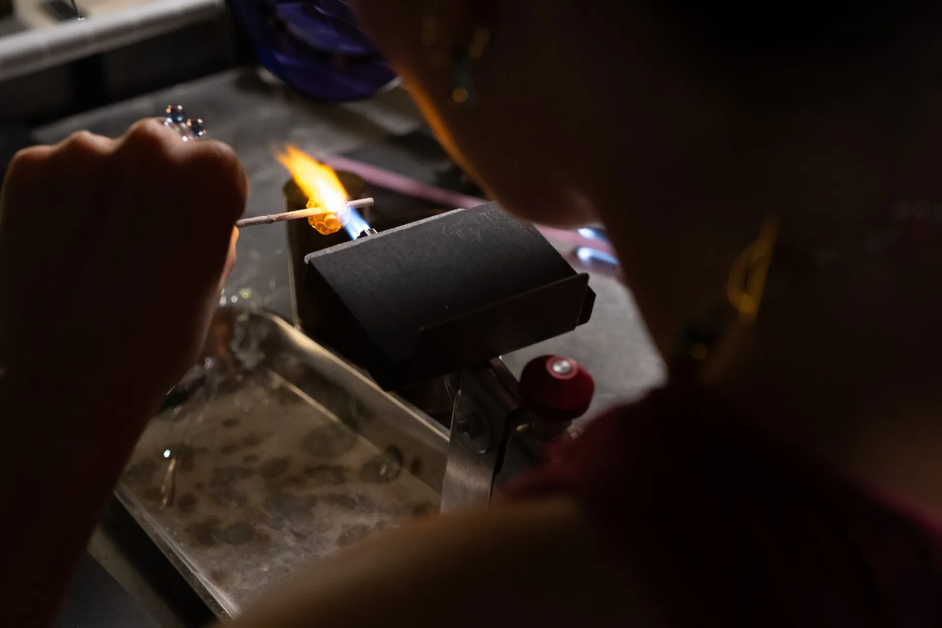 A glowing bead on the mandrel, seen over the artisan’s shoulder