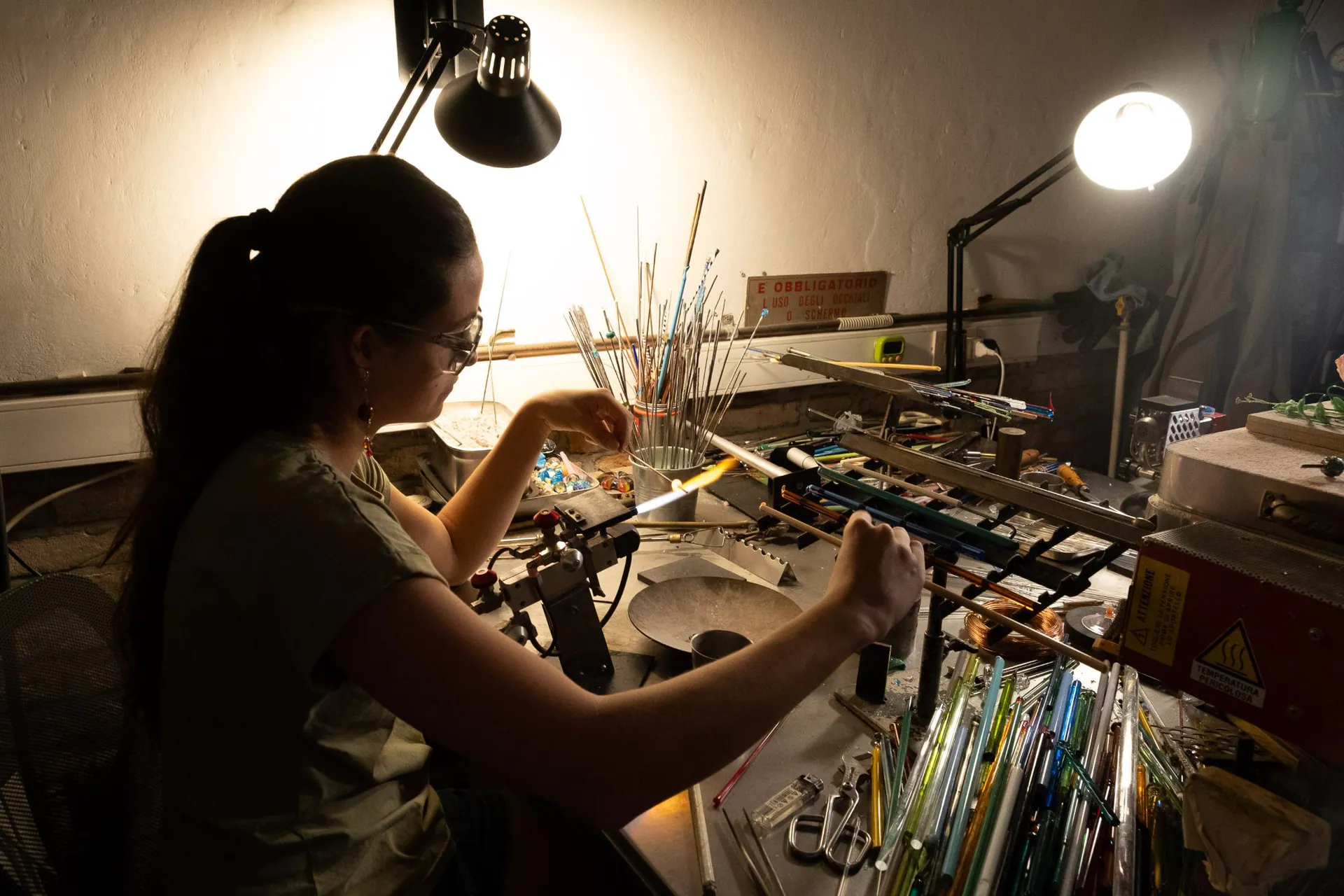 A young artisan at the lamp, surrounded by coloured glass rods