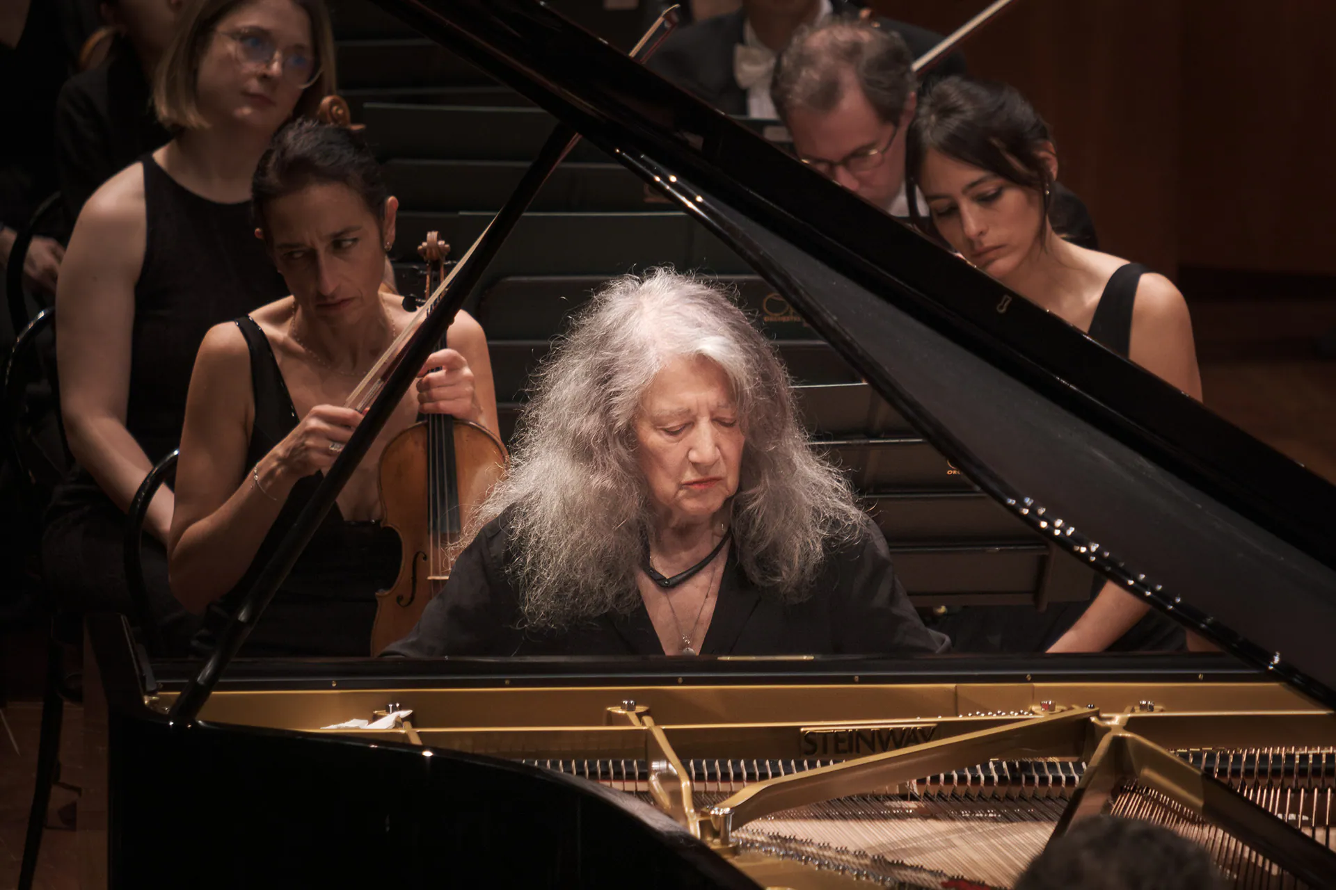 Martha Argerich al pianoforte, concentrata, tra le musiciste dell’orchestra.