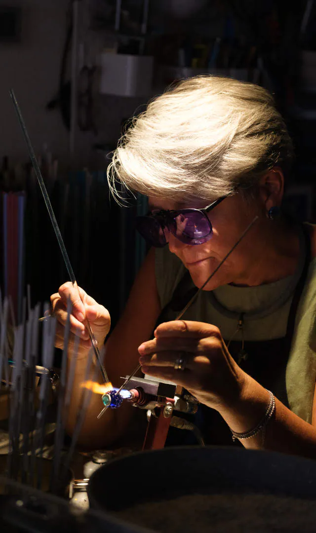 Un’artigiana dai capelli bianchi al lume, a Murano