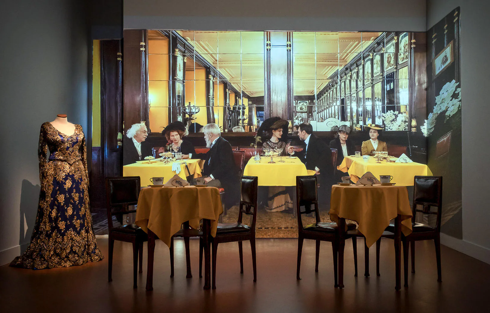 Tavoli apparecchiati e manichino in abito d’epoca davanti alla proiezione di un caffè storico