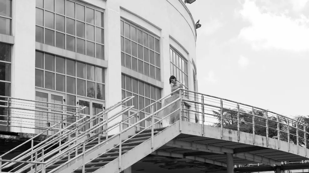 Fotogramma: la protagonista su una scala esterna di un edificio olivettiano