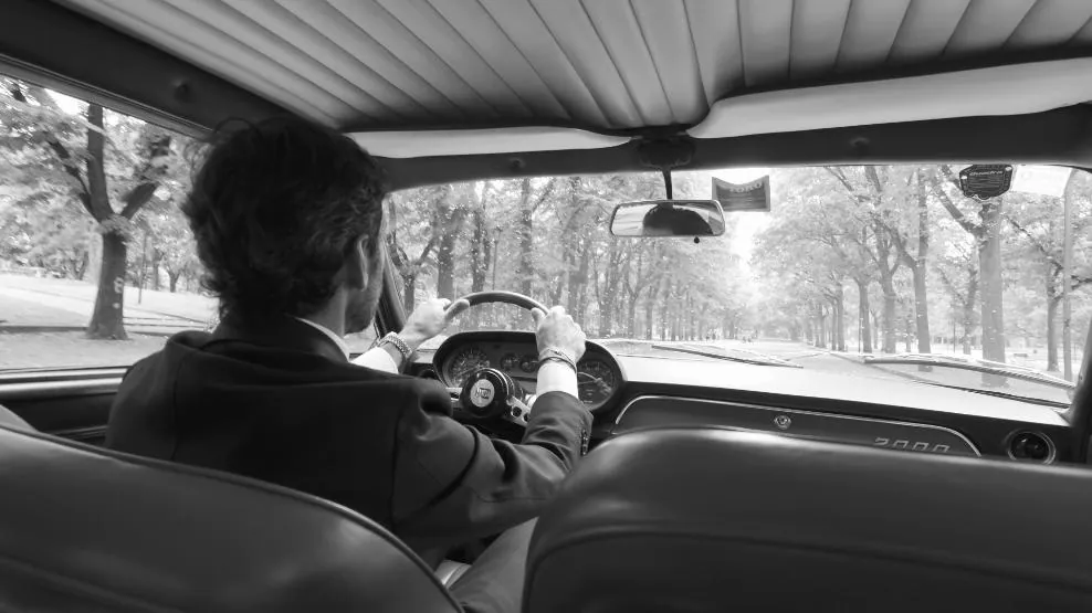 Fotogramma: un uomo alla guida di un’auto d’epoca