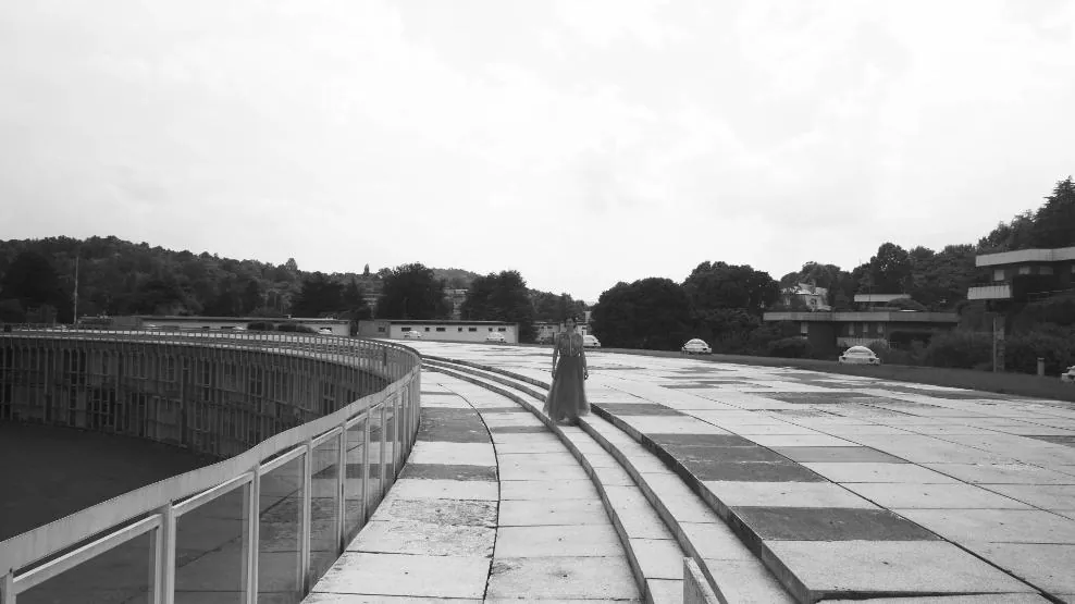 Fotogramma: una figura lontana su un lungo viale curvo di cemento