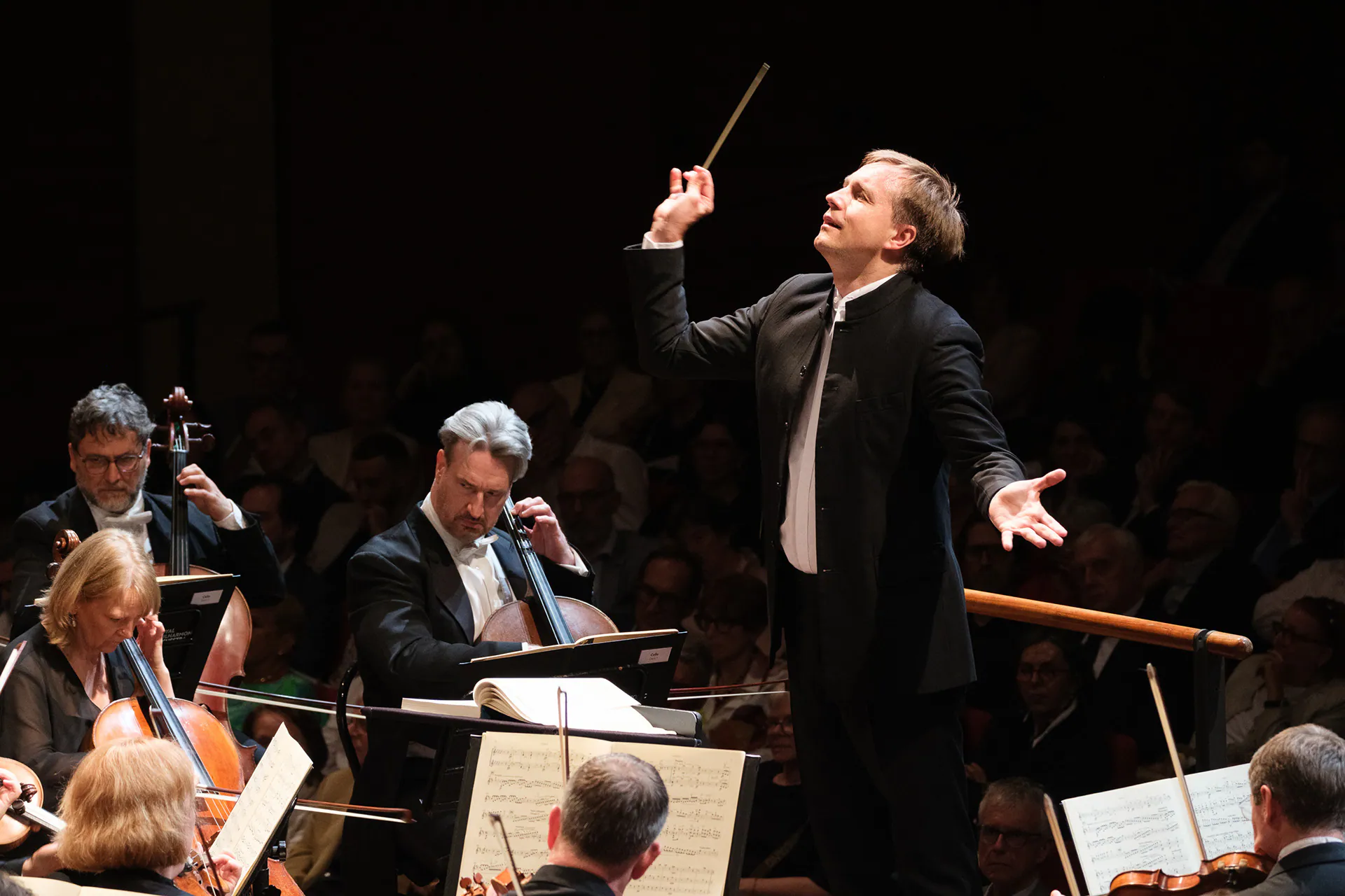 The conductor of the Royal Philharmonic Orchestra, baton raised, in front of the musicians.