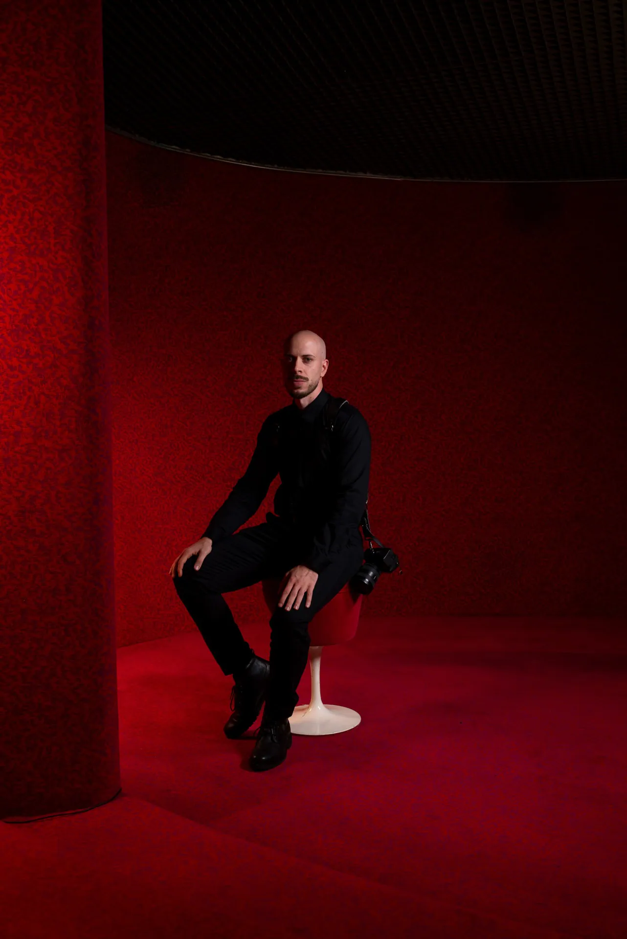 Portrait of Simone Borrasi, filmmaker at Wonderproof Studio, seated with his camera on a shoulder strap